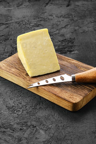 Triangular piece of hard cheese on wooden cutting board