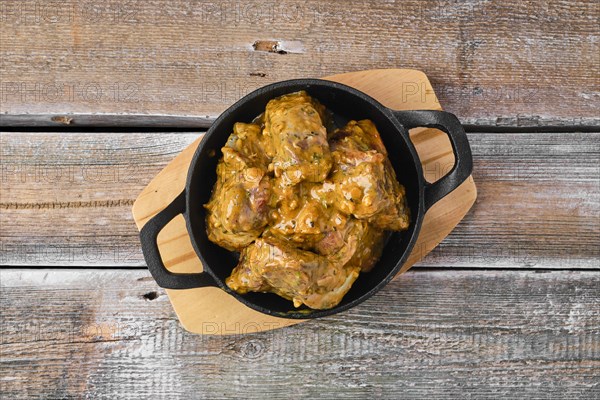 Lamb saddle marinated in mustard in cast iron skillet on wooden table