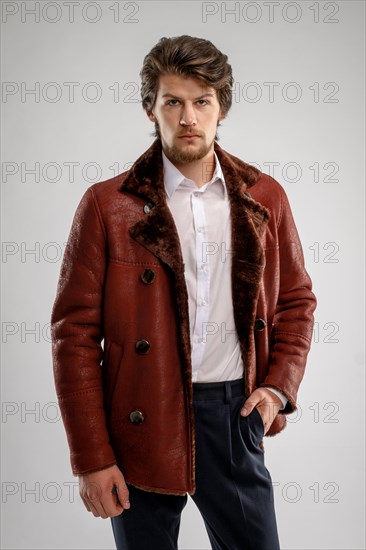 Brutal handsome unshaven man with beard and moustache in sheepskin coat with fur collar