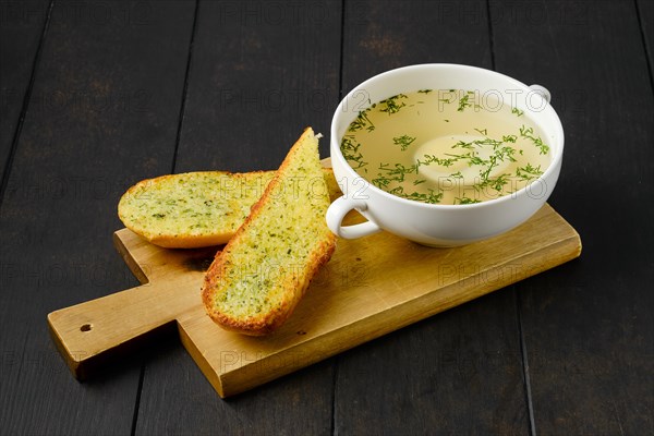 Chicken stock with egg and crispy garlic toasted bread on wooden serving board