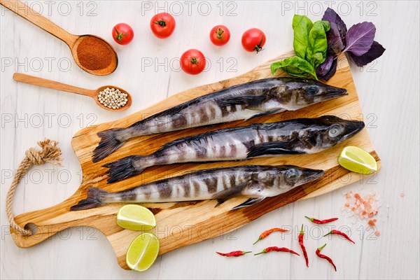 Top view of raw fresh icefish on wooden cutting board with spice and herbs