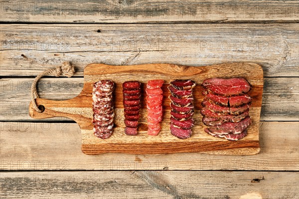 Top view of slices of smoked dried beef and pork meat on wooden cutting board