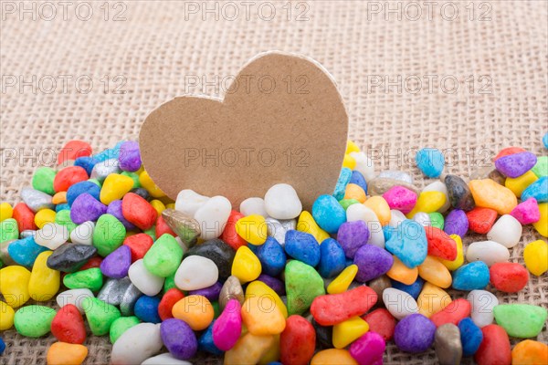 Paper heart amid colorful pebbles on canvas ground