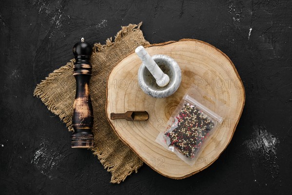 Wooden cross section with mixture of peppers in plastic package and stone mortar and mill