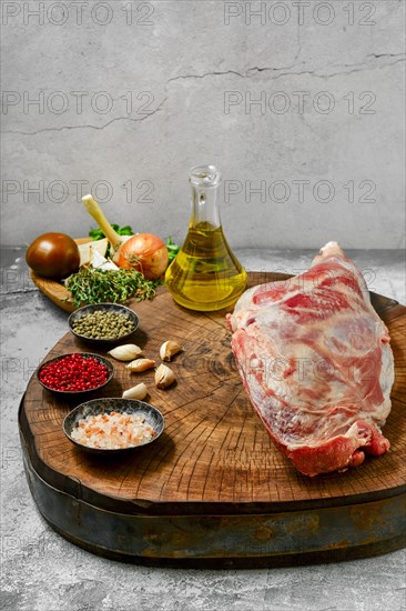 Raw lamb leg chump on with ingredients for cooking on wooden stump