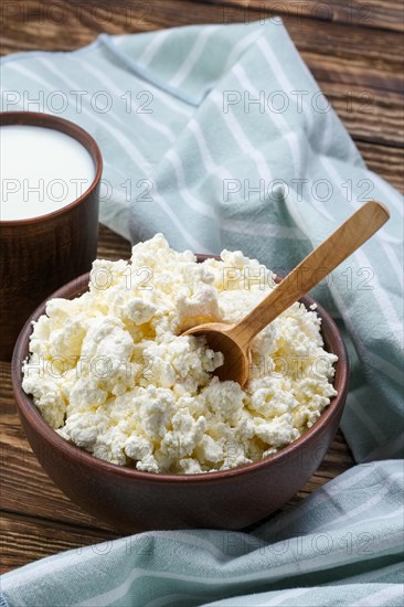 Cottage cheese with wooden spoon in it and milk in clayware on wooden table