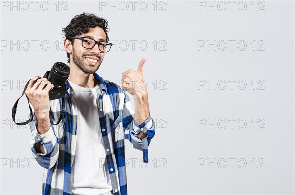 Smiling male photographer showing a camera and giving thumb up. Young man holding a camera and giving the thumb up