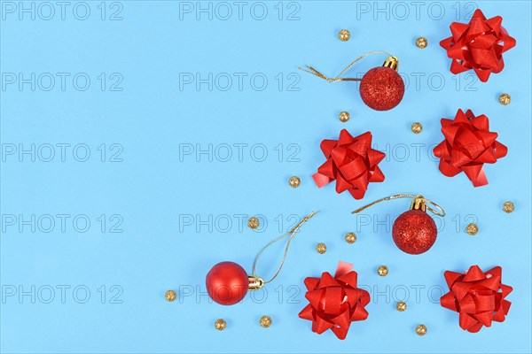 Christmas flat lay with red gift wrapping ribbons and golden ball ornaments and tree baubles on light blue background with empty copy space