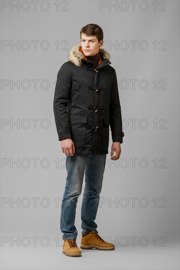 Full length portrait of handsome man in warm coat with hood posing in studio