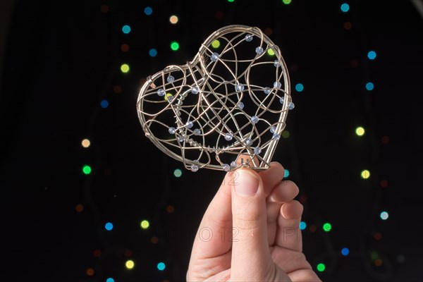 Heart shaped metal cage in hand on bokeh light background