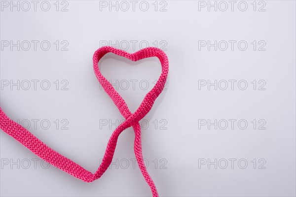 Heart shaped made by the help of a pink sholace on white background