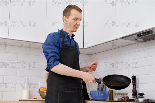 Middle-aged man distributes oil on a hot frying pan