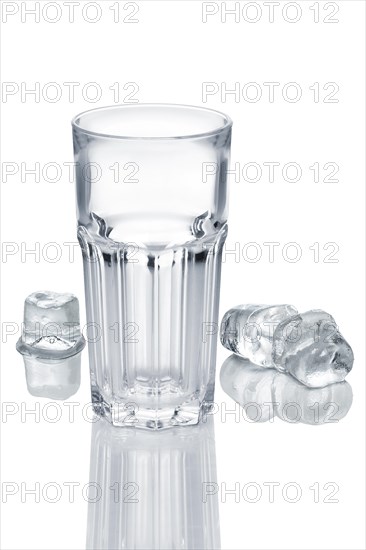 Empty faceted glass and three ice cubes melting on white glass table