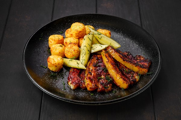 Roasted pork belly with potato balls and pickled cucumber on a plate