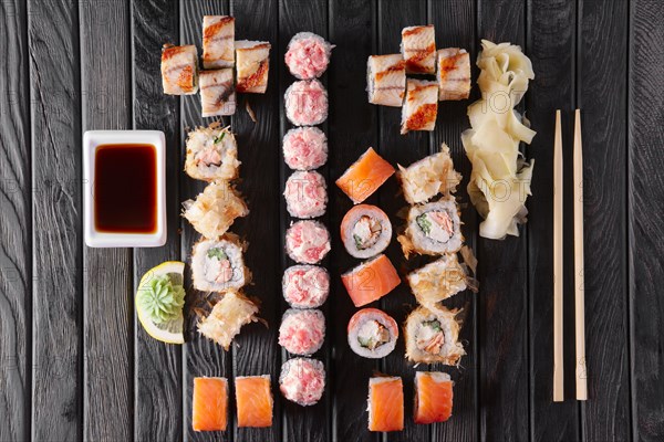 Large set of rolls with garnish and hashi on dark wooden plate