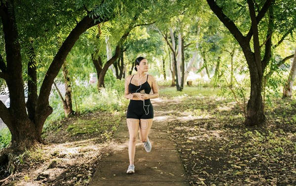 Lifestyle of sporty young woman running in a park surrounded by trees. Healthy lifestyle concept