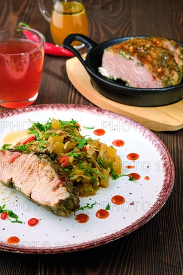 Closeup view of oven-baked meat with braised cabbage and zucchini and hot spicy sauce