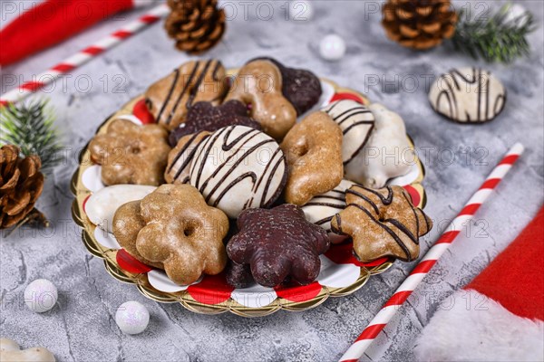 Traditional German gingerbread cookies with sugar and brown and white chocolate glazing in heart and star shape on striped plate surrounded by seasonal Christmas decoration