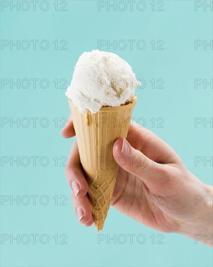 Hand holding vanilla ice cream cone blue background