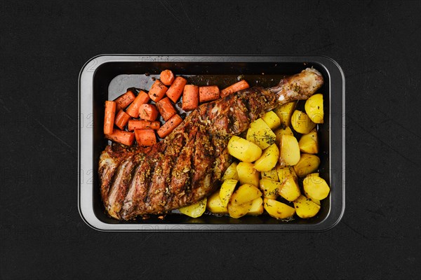 Overhead view of baked in oven lamb shoulder with potato and carrot in oven-tray