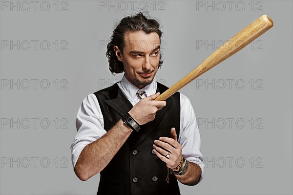 Dramatic man in white shirt and black vest with long curly hair holding baseball bat