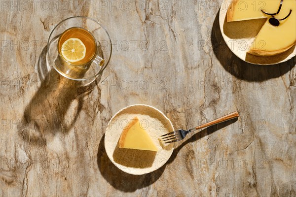 Top view of piece of lemon tart with tea under direct sunlight with hard shadows on the table