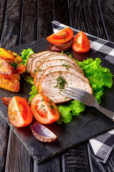 Sliced baked ham with fresh tomatoes on a stone plate in a rustic style