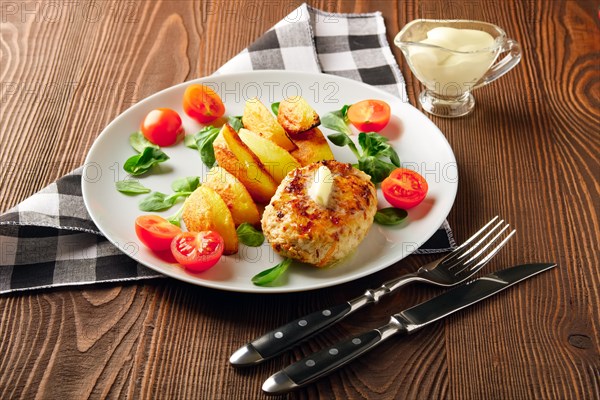 Fried chicken cutlet with potato slices served with tomato cherry and corn salad. Traditional belorussian food