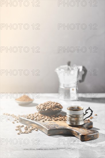 Hot cup of espresso with coffee beans scattered on wooden board and a pot under hard morning sun