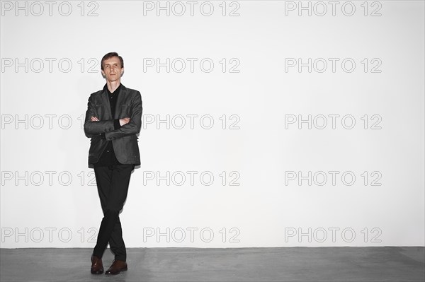 Middle age man in gray wool jacket and brown shoes standing near white concrete wall with crossed hands