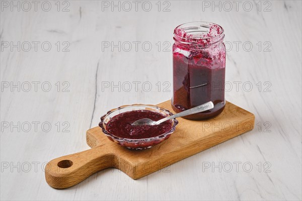 Homemade blueberry jam in a jar and saucer on wooden serving board