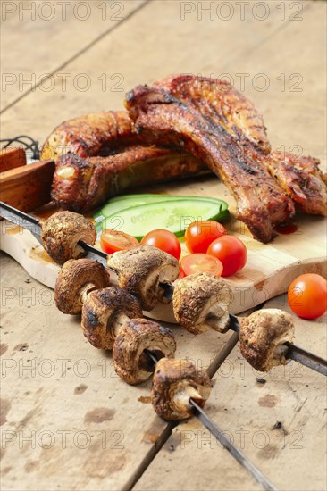 Grilled ribs and champignon on skewer served with fresh cucumber and tomato on wooden table outdoor