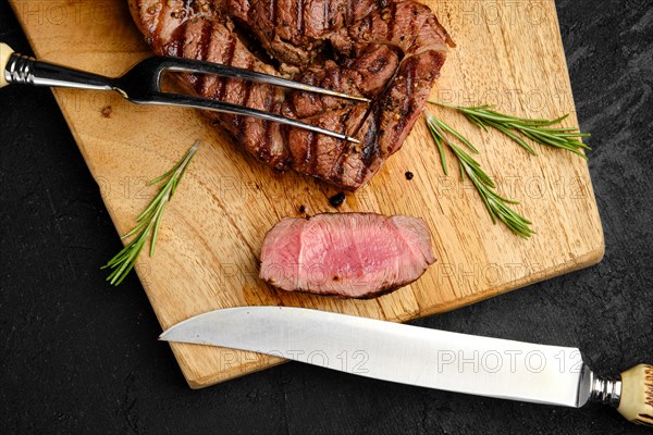 Close up view of juicy steak on wooden cutting board over black background