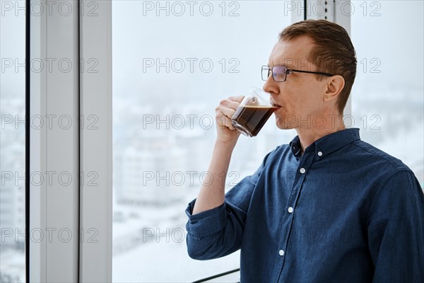 Middle-aged man is standing on balcony and drinking coffe in the early winter morning