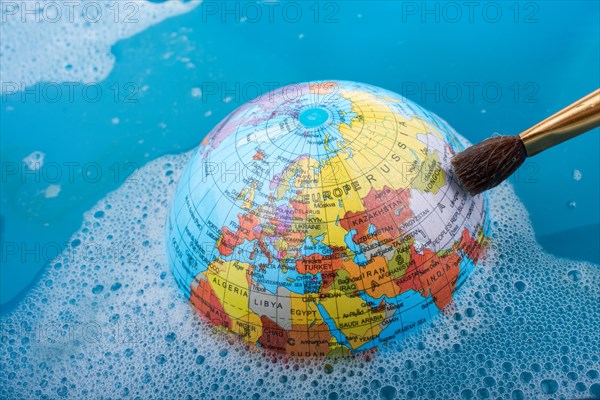 Paint brush placed on the top of globe in a water covered with foam