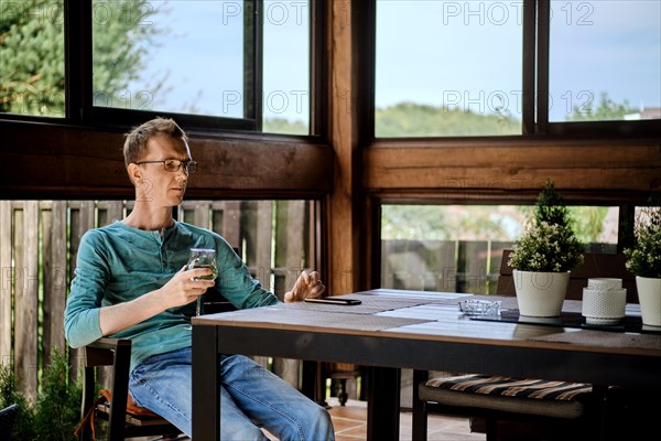 Middle aged man is resting on the veranda with a glass of wine resets an incoming call