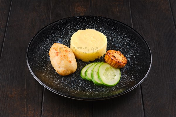 Fried chicken cutlet with mashed potato and slices of fresh cucumber and grilled corn