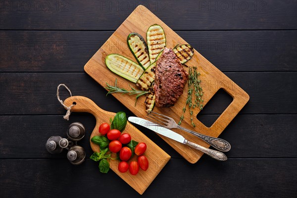 Top view of beef steak and zucchini served with fresh tomato cherry and basil on wooden cutting board