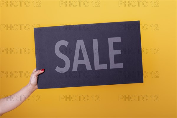 Female hand holding a Sale poster. Studio shot