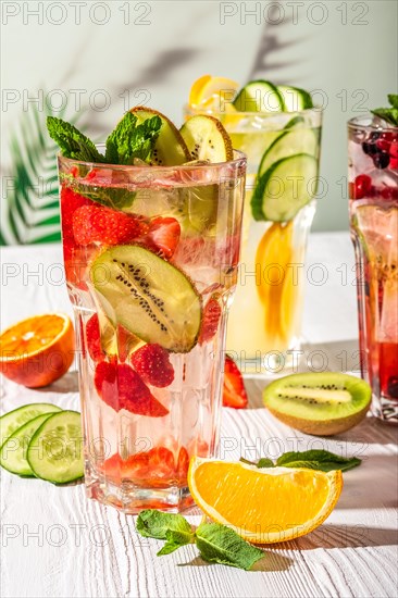 Variations of lemonades with different fruits and syrups on white wooden table under morning sun