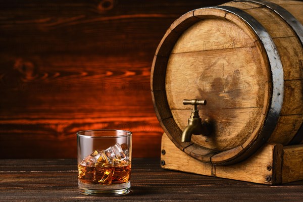 Glass of whisky with ice with barrel on background