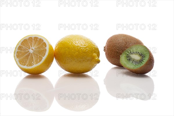 One whole and one half of lemon and kiwi with reflection on white glass table