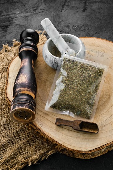 Wooden cross section with Provencal herbs in plastic package and stone mortar and mill