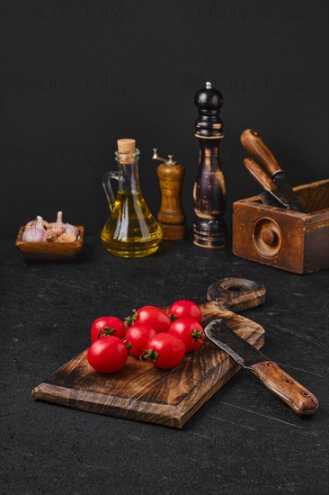Fresh small whole tomatoes on wooden cutting board on rustic kitchen table