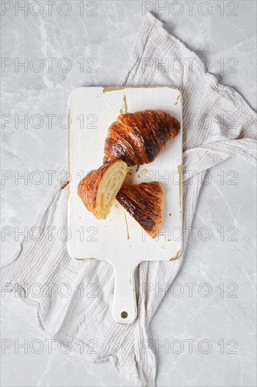 Top view of classic croissant cut on half on white wooden serving board