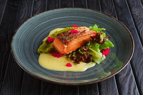 Fried salmon fillet with salad leaves and cream sauce decorated with caviar