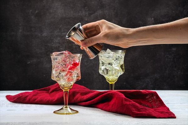 Hand of bartender with jigger pouring pomegranate bitter in cocktail with gin