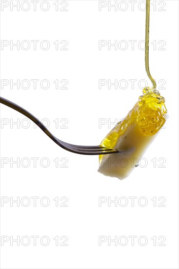 Piece of cheese on fork with floating honey