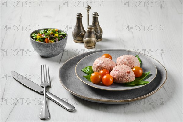 Semifinished frozen veal meatballs on a plate with basil and tomato