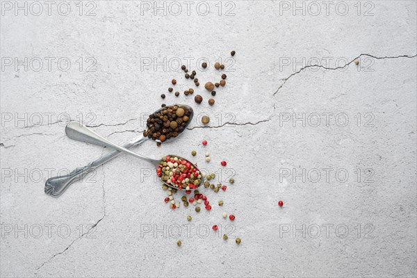 Two crossed spoons with different kinds of pepper on concrete background